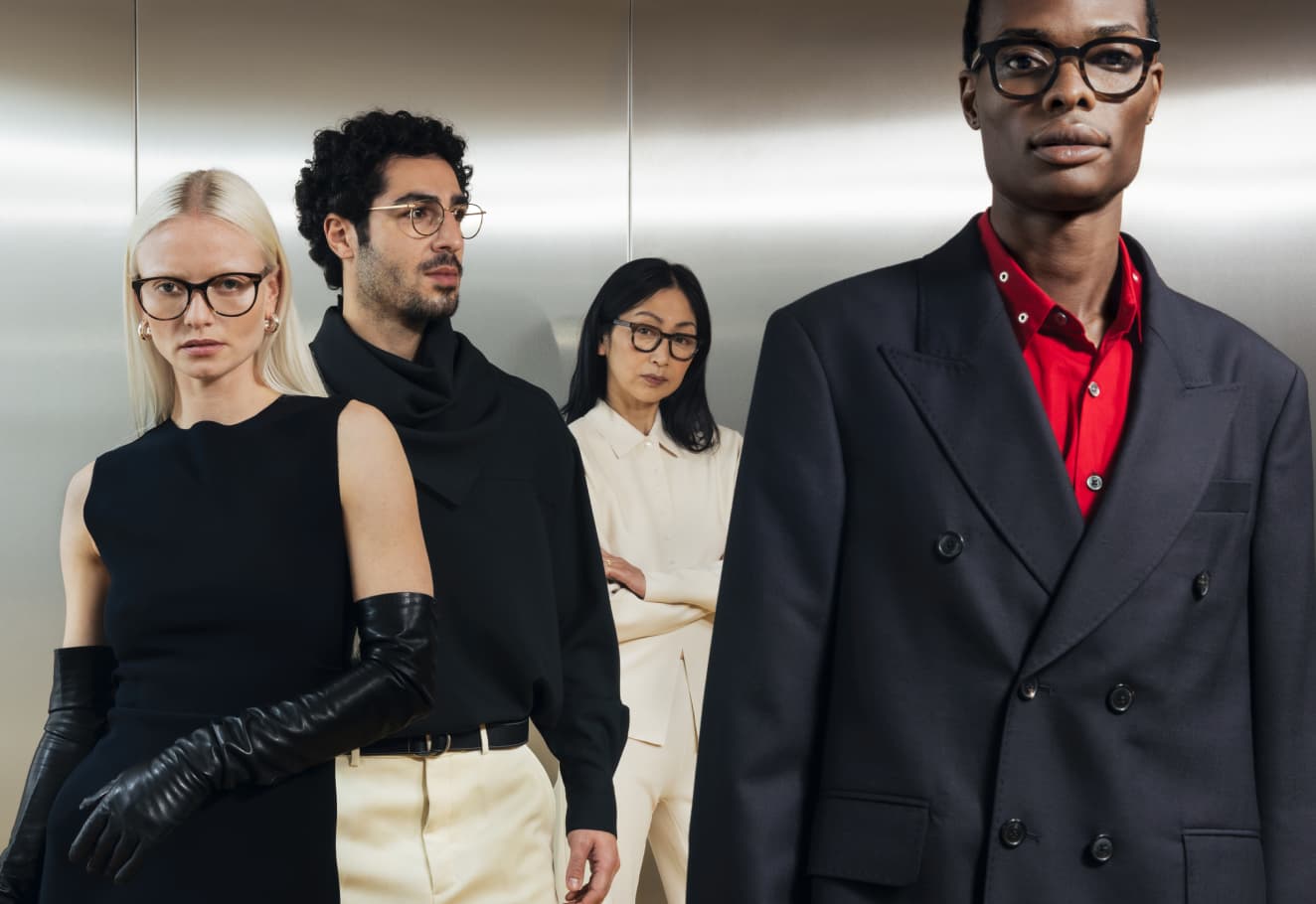 Ace & Tate | Four models wearing various styles of glasses standing in a row against a metallic silver background.